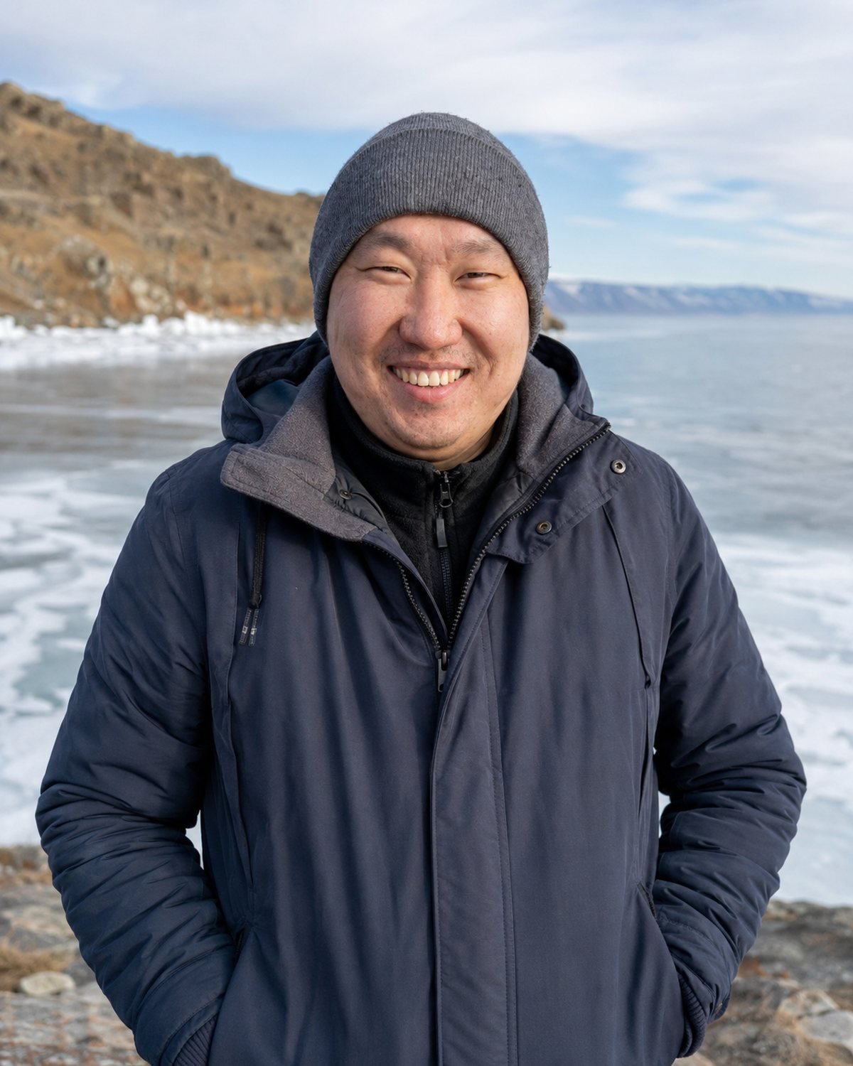 Denis Sobakin smiling on the frozen shore of Lake Baikal in winter, ice stretching to the far mountains behind him