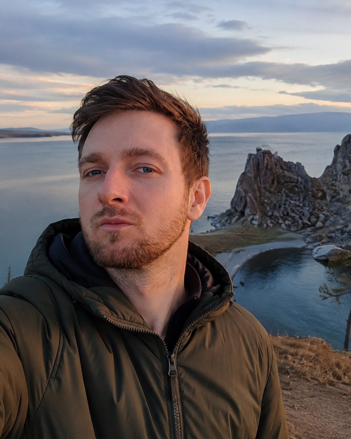 Aleksandr Kovalev at Cape Burkhan on Olkhon Island at sunset, Shaman Rock and the water of Lake Baikal behind him